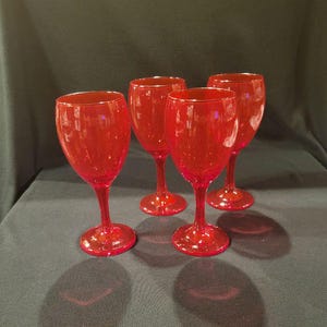 May include: Four red wine glasses with a textured surface. The glasses have a classic stem and base design. The glasses are made of a transparent material, allowing light to pass through. The glasses are arranged on a dark surface.