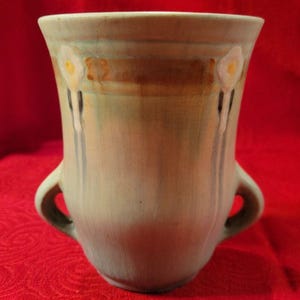 May include: A green ceramic vase with two handles and a floral design. The vase has a light green glaze with brown and white accents.