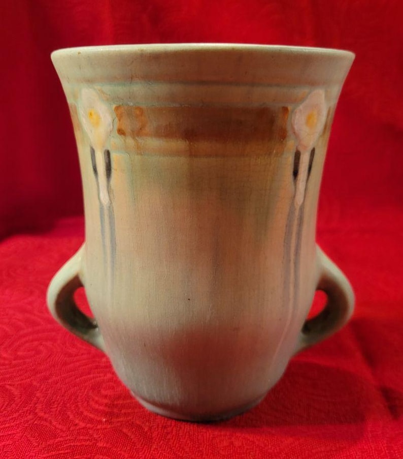 May include: A green ceramic vase with two handles and a floral design. The vase has a light green glaze with brown and white accents.