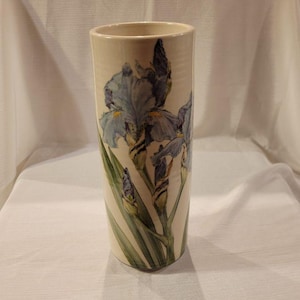 May include: A white ceramic vase with a blue and green floral design. The vase features a hand-painted design of irises with green leaves.