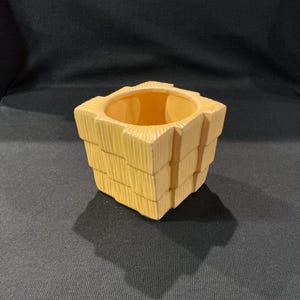 May include: A yellow ceramic planter with a geometric, stacked design. The square-shaped planter has a textured, ribbed surface and a wide opening. The interior of the planter is a lighter shade of yellow. The planter is suitable for small plants or decorative use.