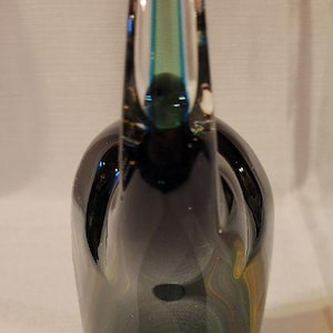 May include: A dark green glass decorative bottle with a long neck and a small handle. The bottle has a rounded base and a clear glass top with blue and green accents. The glass has a glossy finish.