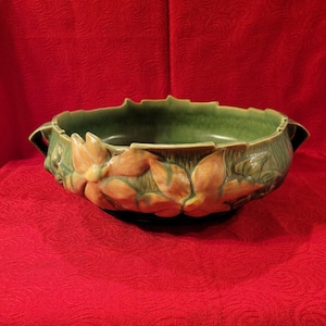 May include: A green glazed ceramic bowl with two handles and a floral design. The bowl features raised, sculpted flowers in shades of orange and yellow.