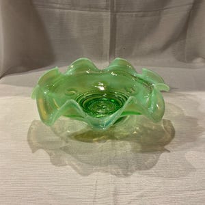 May include: A green glass bowl with a scalloped edge and a raised center. The bowl is made of iridescent glass and has a vintage look.