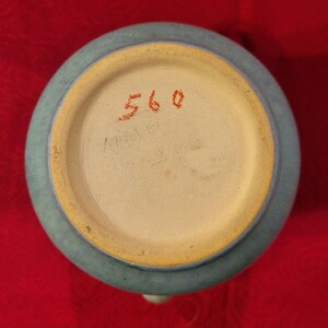 Pu&ograve; includere: Il fondo di un vaso in ceramica blu chiaro con un bordo giallo. Il numero 560 &egrave; scritto in rosso sul fondo.