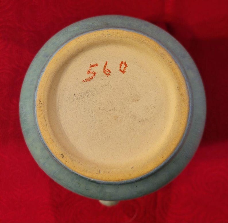 Pu&ograve; includere: Il fondo di un vaso in ceramica blu chiaro con un bordo giallo. Il numero 560 &egrave; scritto in rosso sul fondo.