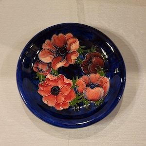 May include: A blue ceramic plate with a floral design featuring four red and pink anemones with green leaves.