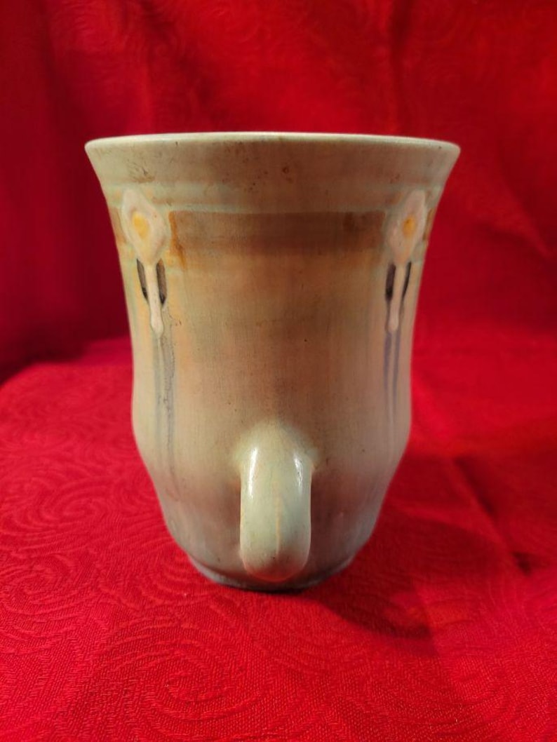 May include: A light blue ceramic vase with a white floral design and two handles. The vase has a glazed finish and a slightly iridescent sheen.