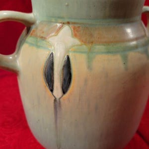 Pu&ograve; includere: Un vaso in ceramica verde smaltato con due manici e un design floreale stilizzato in bianco, marrone e nero.