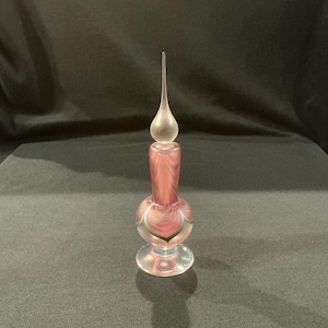 May include: A pink and white glass bottle with a clear glass stopper. The bottle has a swirl design and a round base.