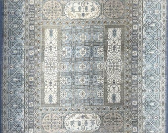 Puede incluir: Una alfombra rectangular azul claro con un patrón simétrico intrincado. El diseño presenta motivos florales y geométricos en tonos de azul, beige y gris. La alfombra tiene un borde detallado y un medallón central, creando un aspecto clásico y elegante.