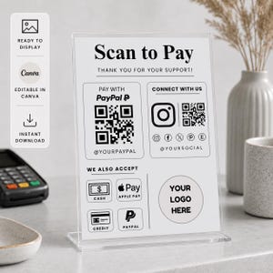 May include: A clear acrylic sign holder displaying a white payment information card with black text and icons. The card features the heading Scan to Pay, a PayPal QR code, social media icons, and sections for payment methods including Apple Pay.