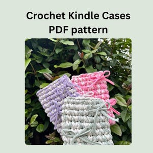 May include: Three crochet Kindle cases in shades of lavender, pink, and green, each with a matching ribbon tie. The cases are displayed against a backdrop of green foliage. The text "Crochet Kindle Cases PDF pattern" is at the top.