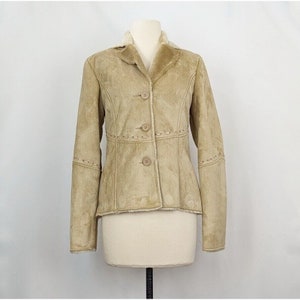 Puede incluir: Una chaqueta de ante marrón con cuello de piel sintética y cierre de botones. La chaqueta tiene costuras decorativas en las mangas y la cintura.