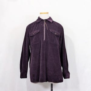Peut inclure: Une chemise en velours côtelé violet avec une fermeture éclair et deux poches à rabat. La chemise a des manches longues et un col.