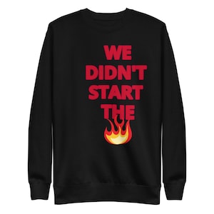 Peut inclure: Sweat-shirt noir avec un texte rouge qui dit "We didn't start the fire" avec un graphique de flamme orange stylisé en dessous.