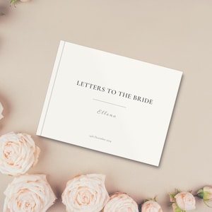 May include: A white book with the text "Letters to the Bride" and the name "Elena" on the cover. The book is surrounded by pale pink roses.