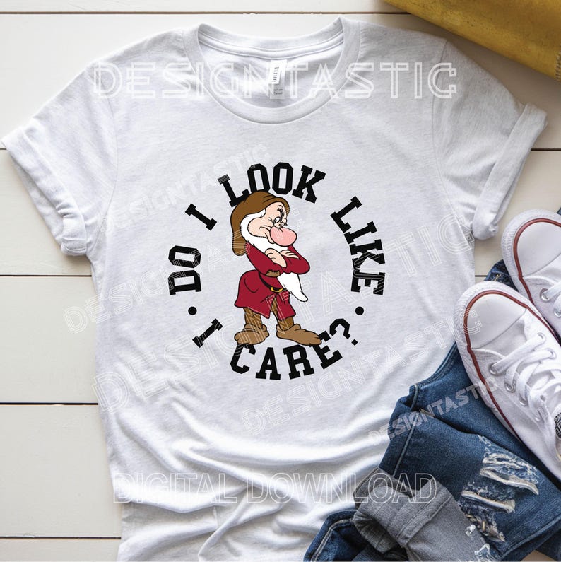 May include: White t-shirt with a cartoon image of Grumpy from Snow White, and the text "I DO LOOK LIKE I CARE?". The design is in black, red, brown, and beige. The shirt is shown with blue jeans and white trainers.
