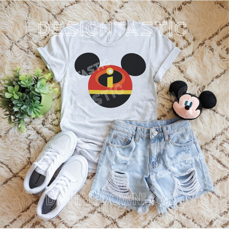 May include: A white t-shirt with a black and red Mickey Mouse head design featuring the Incredibles character, Mr. Incredible. The design includes a red circle with a yellow 'I' and a black outline. The shirt is paired with light blue denim shorts and white sneakers.