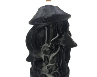 May include: Black mushroom-shaped incense burner with a brown incense cone at the top. The burner has a detailed design with multiple mushroom caps and a flowing smoke effect. The product is designed to hold incense cones.