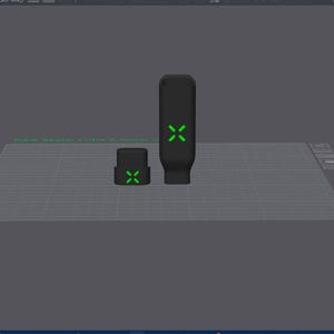 May include: Two black, rectangular objects with green cross-shaped designs. One is tall and cylindrical, the other is shorter and square. The objects are on a grey surface.