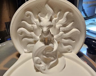 May include: A white, 3D-printed sculpture of a fox with multiple tails, sitting atop a swirling base. The fox is centered within a circular frame with detailed, flowing patterns. The base has a sun design.