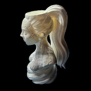 May include: A white, 3D-printed bust of a woman's head and shoulders, featuring a ponytail and a vessel-like opening at the top. The sculpture has detailed facial features and a textured surface, set against a black background.