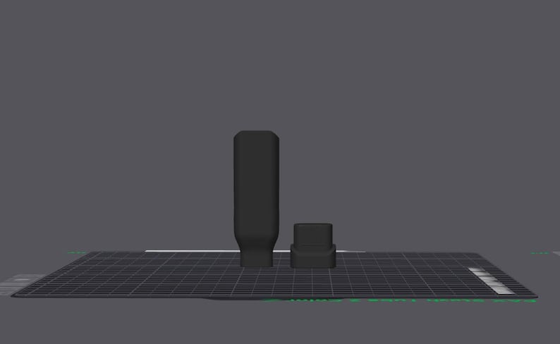 May include: Two black objects, one cylindrical and one square, on a dark grey grid. The cylindrical object has a rectangular base. The background is a solid grey. The objects appear to be 3D models.