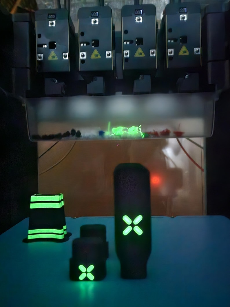 May include: Several black objects with glowing green details, including a rectangular shape, two small cubes, and a tall, cylindrical item. They are on a blue surface, with a complex machine above.