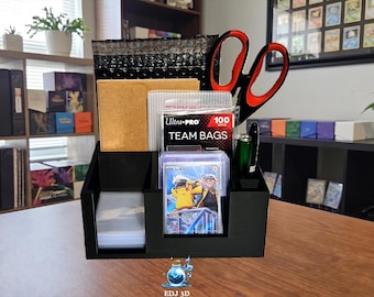 May include: A black plastic desk organizer holding various supplies including a pack of Ultra-Pro Team Bags, a stack of clear card sleeves, a pair of red and black scissors, a green pen, and a trading card featuring a yellow character.