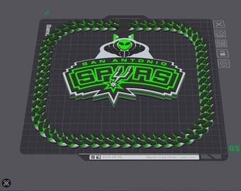 May include: A 3D printed San Antonio Spurs logo emblem in black, white, and neon green, featuring an alien head graphic above the text. The emblem is surrounded by a continuous chain-link border on a digital build plate interface.