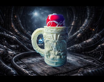 May include: A cream-colored, 3D-printed mug with a detailed, biomechanical design, holding a red Coca-Cola can. The mug features a handle and sculpted figures. The background is a dark, industrial setting with metallic structures. The text "EDJ 3D" is visible.