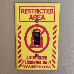 May include: A rectangular yellow light switch cover plate featuring red text that reads RESTRICTED AREA and AUTHORIZED PERSONNEL ONLY, with a red graphic of a locked padlock inside a circle and the word DANGER at the bottom, secured by two screws.