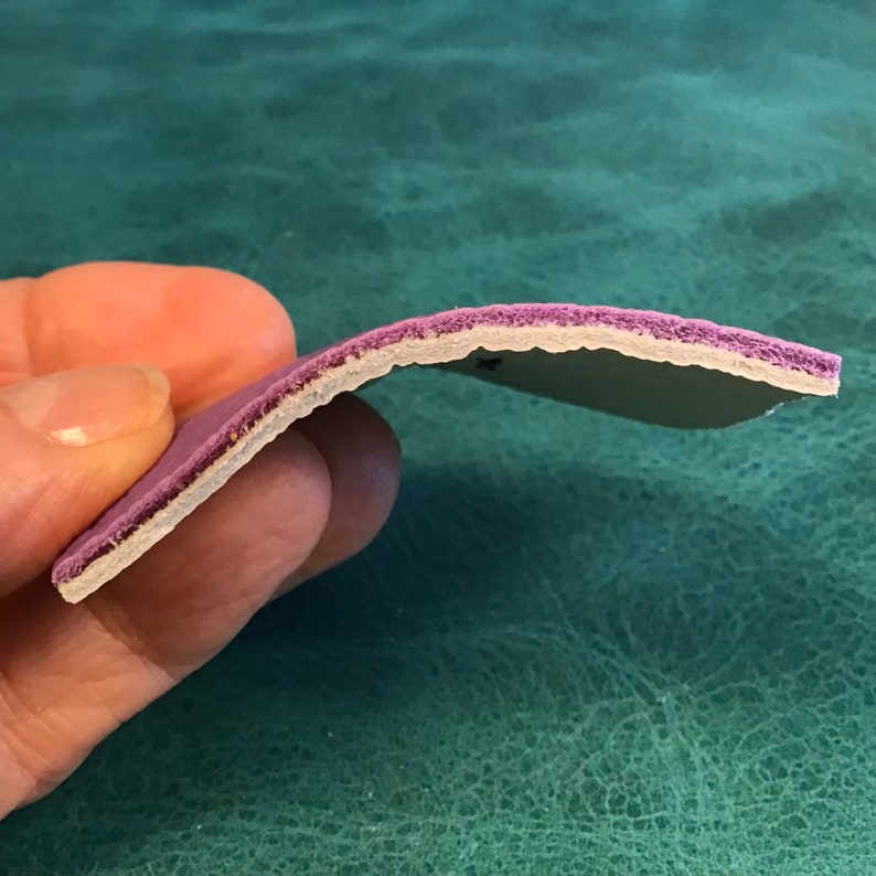 Puede incluir: Primer plano del lado de un material de cuero morado con una capa blanca debajo. El material es flexible y tiene una superficie ligeramente texturizada.