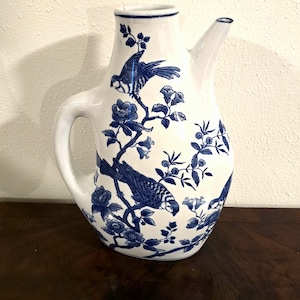 May include: White ceramic pitcher with a curved handle and spout. The pitcher is decorated with blue floral and bird motifs. The design features detailed illustrations of birds perched on flowering branches. The pitcher has a classic, elegant shape.