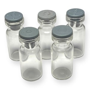 May include: Five clear glass bottles with gray screw-on caps. The bottles are all the same size and shape.
