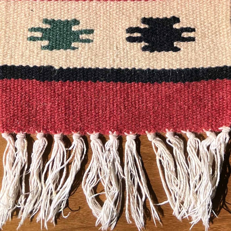 May include: A red, white, and black woven rug with a fringe border. The rug has a geometric pattern with green and black shapes.