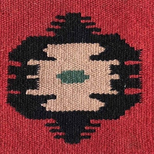 May include: A close-up of a woven rug with a black and brown geometric design. The center of the design features a green square.