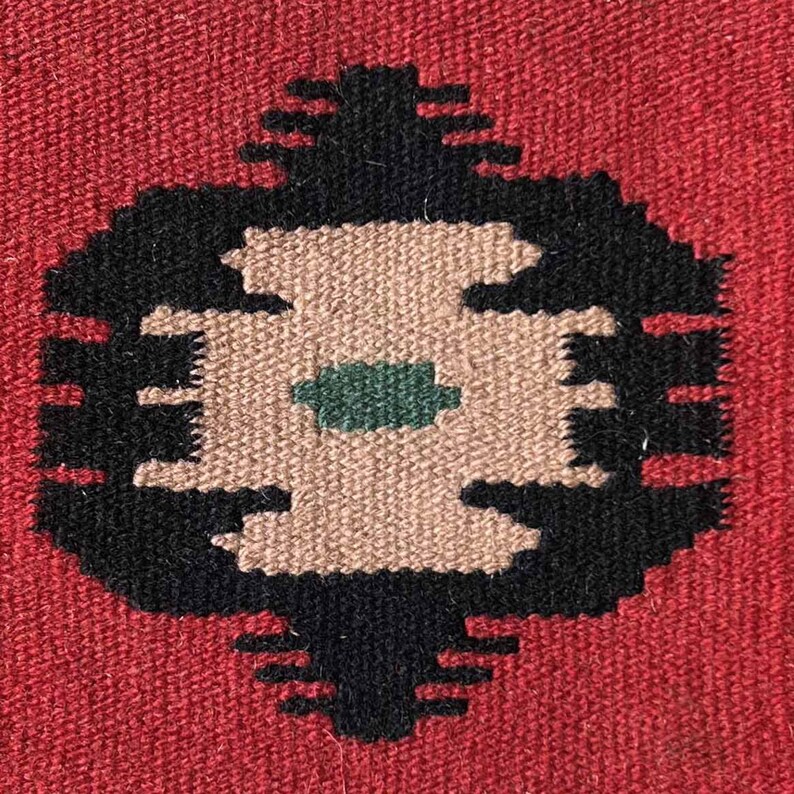 May include: A close-up of a woven rug with a black and brown geometric design. The center of the design features a green square.