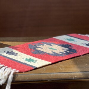 May include: A red, white, and blue woven rug with a geometric pattern. The rug has fringe on the ends.