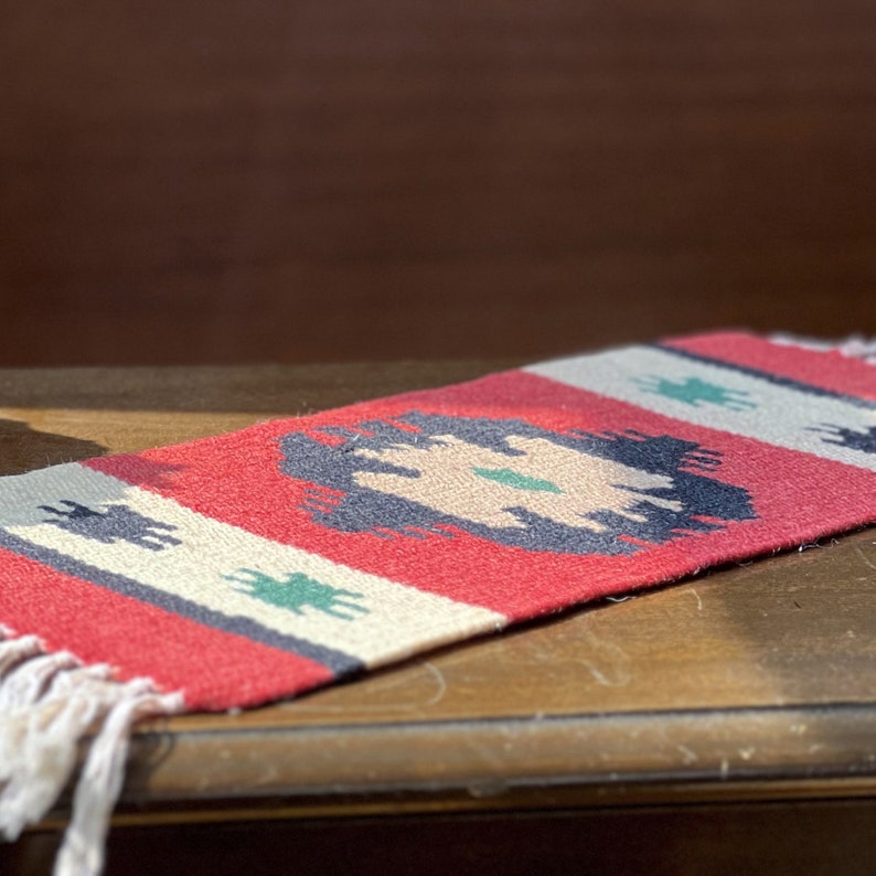May include: A red, white, and blue woven rug with a geometric pattern. The rug has fringe on the ends.