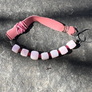 May include: Pink leather keychain with a silver ring and a row of pink and white square beads.