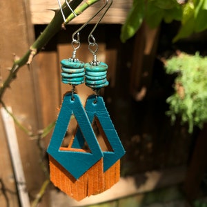 May include: Teal leather earrings with a triangle cutout design and brown fringe. The earrings are accented with turquoise-coloured beads.