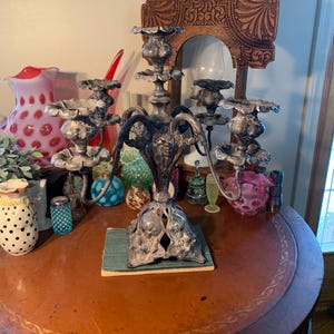 May include: A silver candelabra with five arms and ornate floral details. The candelabra is sitting on a wooden table with a book and other decorative items.
