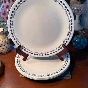 May include: White ceramic plates with a blue diamond and text design. The plates have the words "cafe mocha", "cappuccino", and "cafe latte" around the rim. The plates are stacked on a wooden stand.