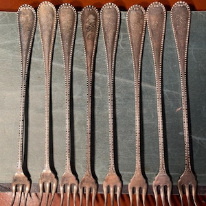 May include: Set of eight silver-plated forks with ornate handles and beaded edges. The forks have three tines each.