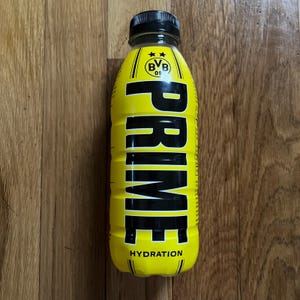 May include: A yellow PRIME hydration drink bottle with black text and a black cap. The bottle has the text "PRIME" in large, bold letters and the word "HYDRATION" at the bottom. The bottle also features a logo.