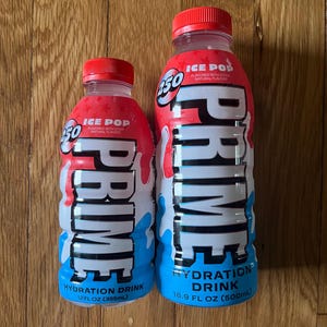May include: Two bottles of PRIME hydration drink, one 12 fl oz and one 16.9 fl oz, with red caps and a red, white, and blue design. The bottles are labeled "ICE POP" and "HYDRATION DRINK". The larger bottle contains 500ml.