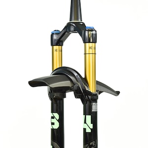 May include: A black bicycle suspension fork featuring gold-colored stanchions, a black mudguard attached to the bridge, and blue adjustment knobs. The lower legs display the number 34 in large light green font with technical text labels.