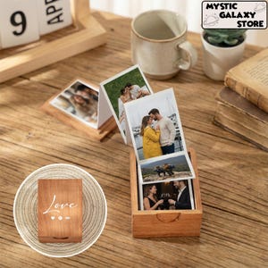May include: A wooden photo box displaying printed photographs. The box is open, revealing several images. A smaller wooden box with the word "Love" is also visible. A calendar and a mug are in the background.